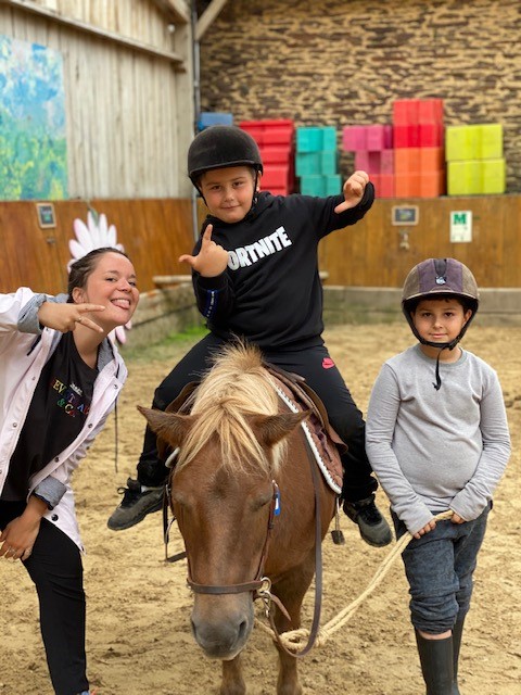 1 enfant sur un poney est entouré de 2 camarades. Tous les trois sourient et posent pour la photo.