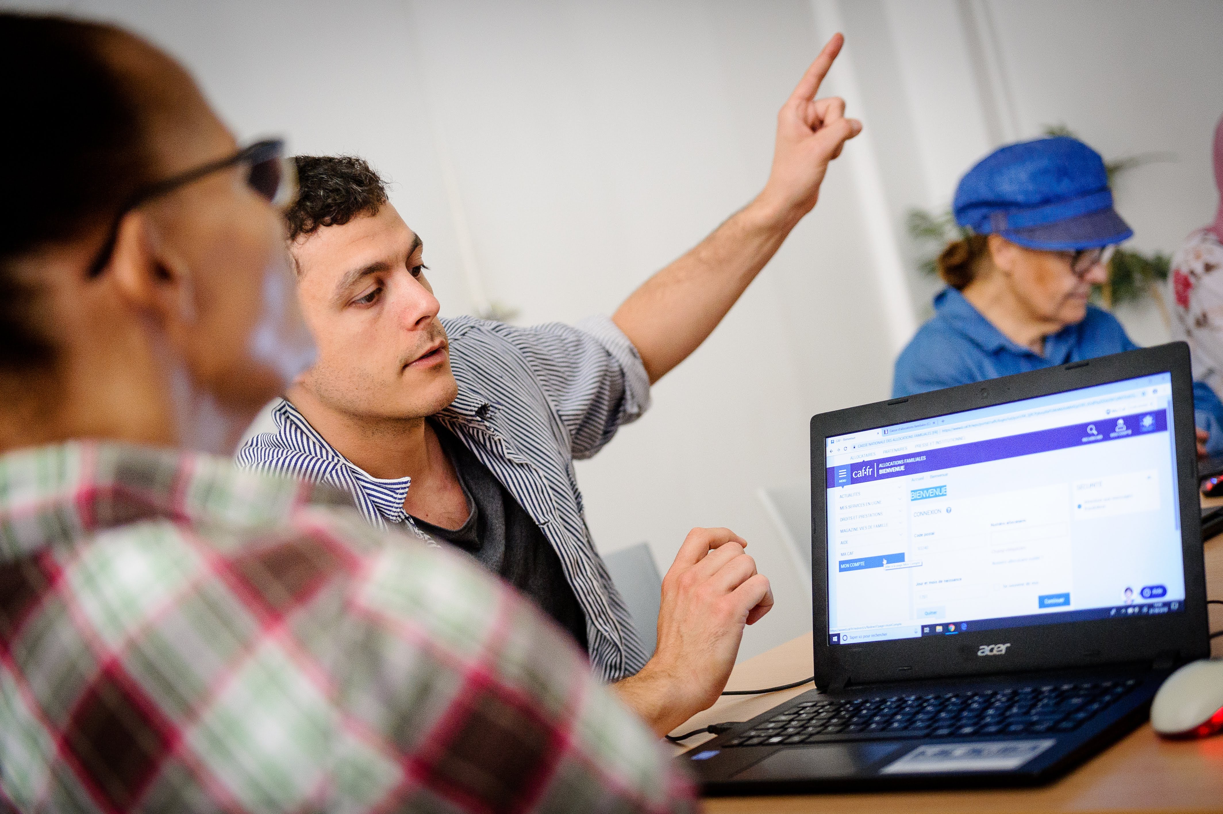 Un jeune m&eacute;diateur num&eacute;rique fait un atelier avec deux personnes &acirc;g&eacute;es, avec un ordinateur chacune pour s'exercer, &agrave; Emmaus Connect.