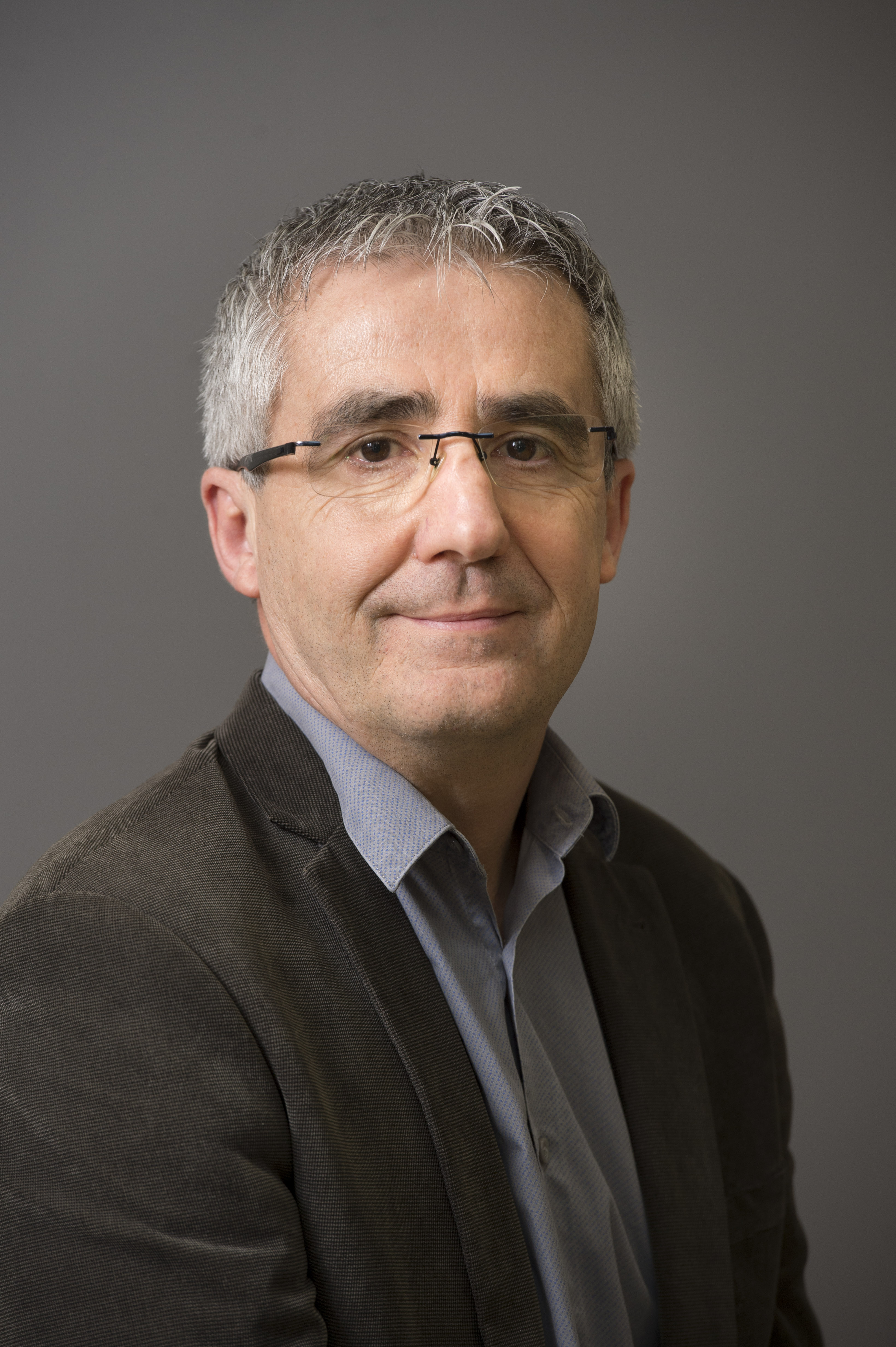 Photo portrait de Dominique Dhumeaux, cheveux gris, lunette, verste marron, chemise grise et cravate fonc&eacute;e