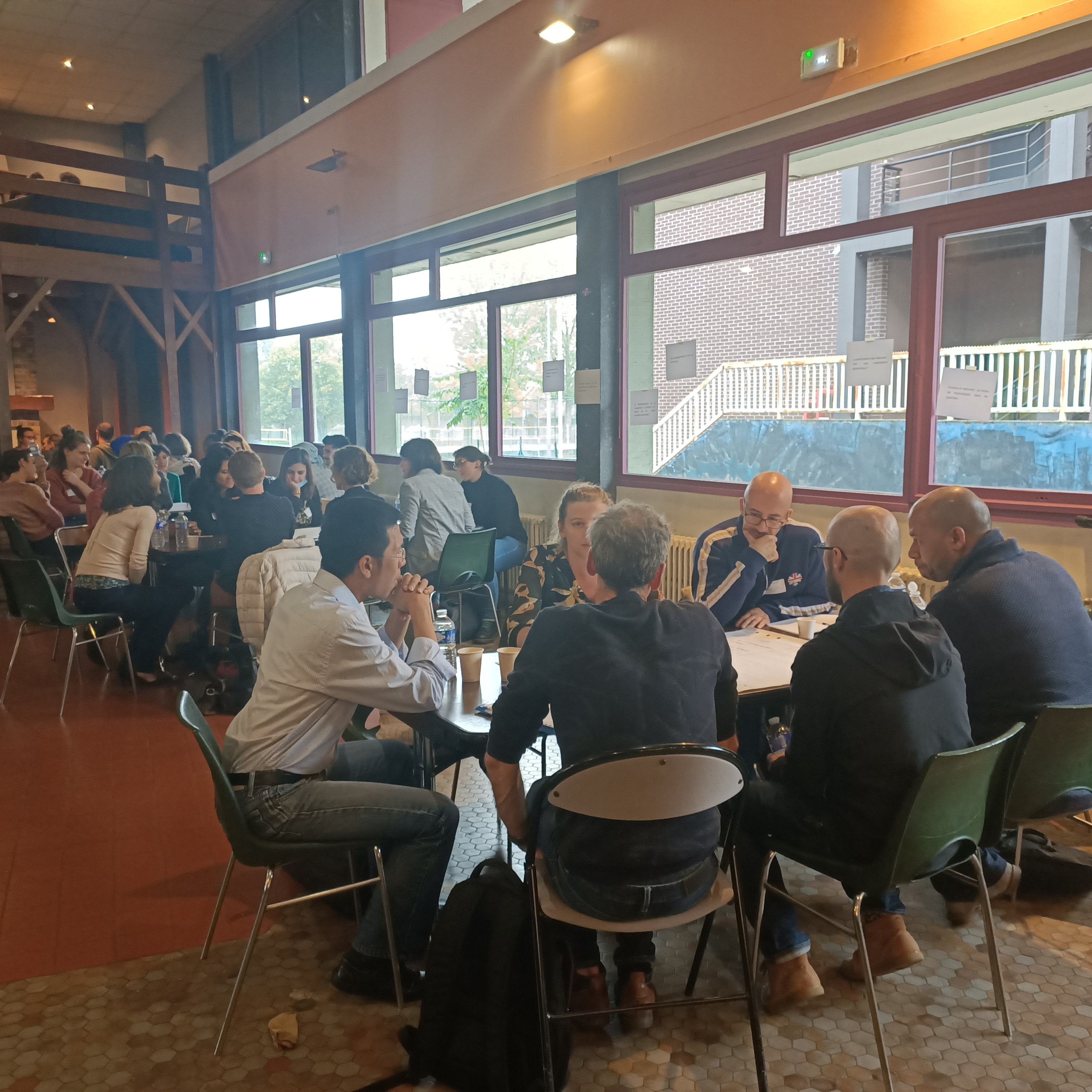 Personnes en atelier de travail, r&eacute;parties dans une grande salle, autour de tables diff&eacute;rentes