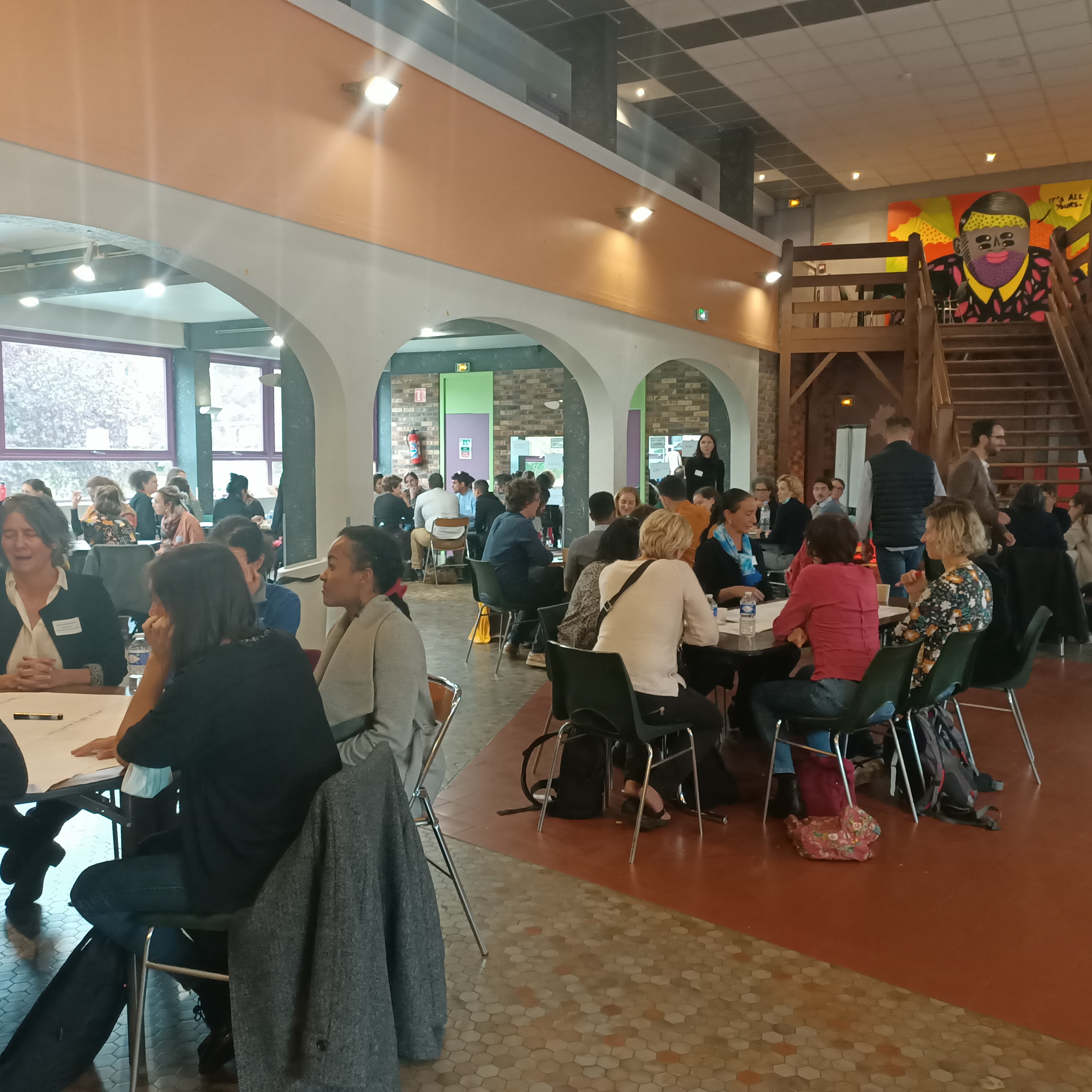 Personnes en atelier de travail, r&eacute;parties dans une grande salle, autour de tables diff&eacute;rentes
