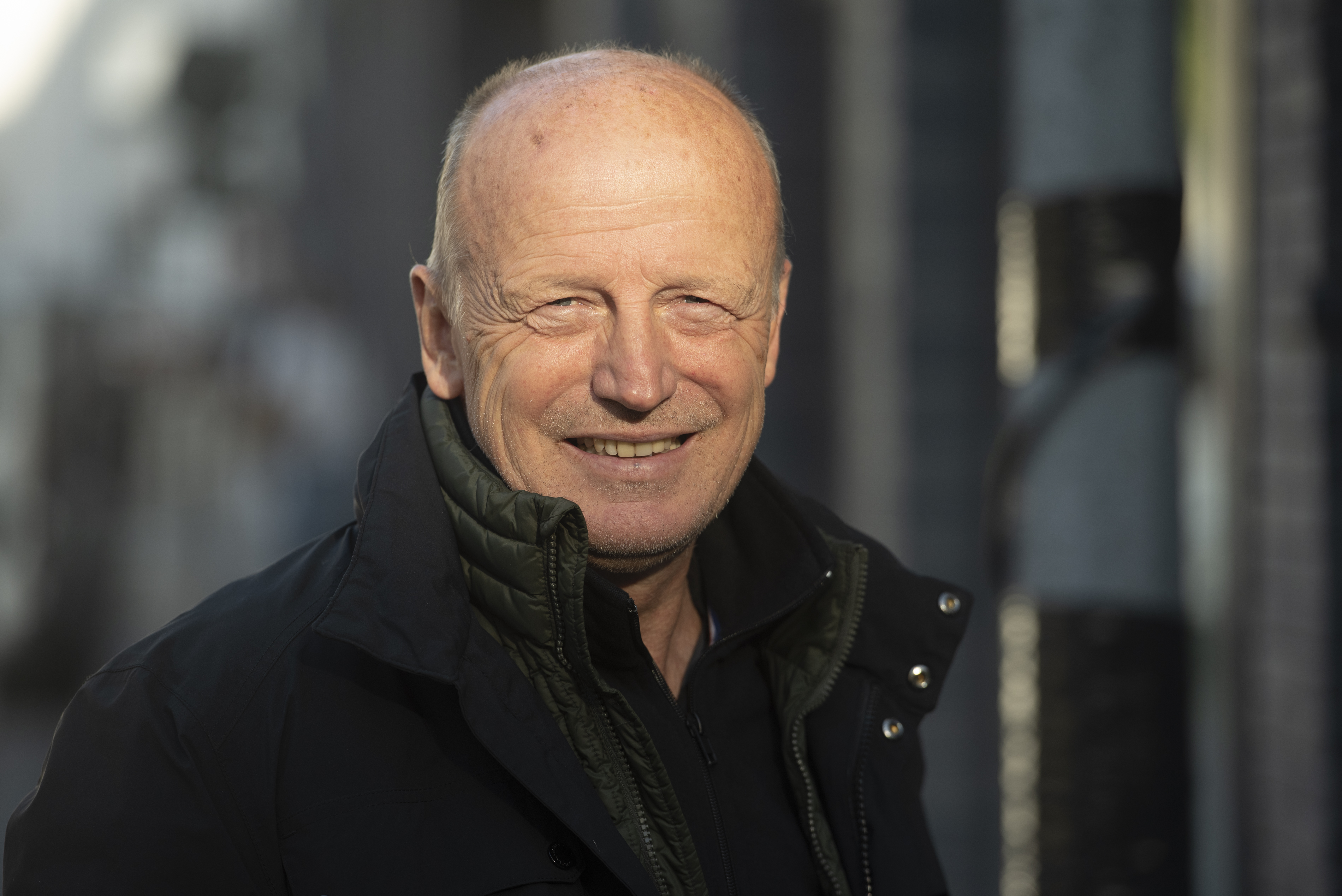 Portrait Bruno Pomart, souriant, cr&acirc;ne ras&eacute;, la soixantaine, veste fonc&eacute;e