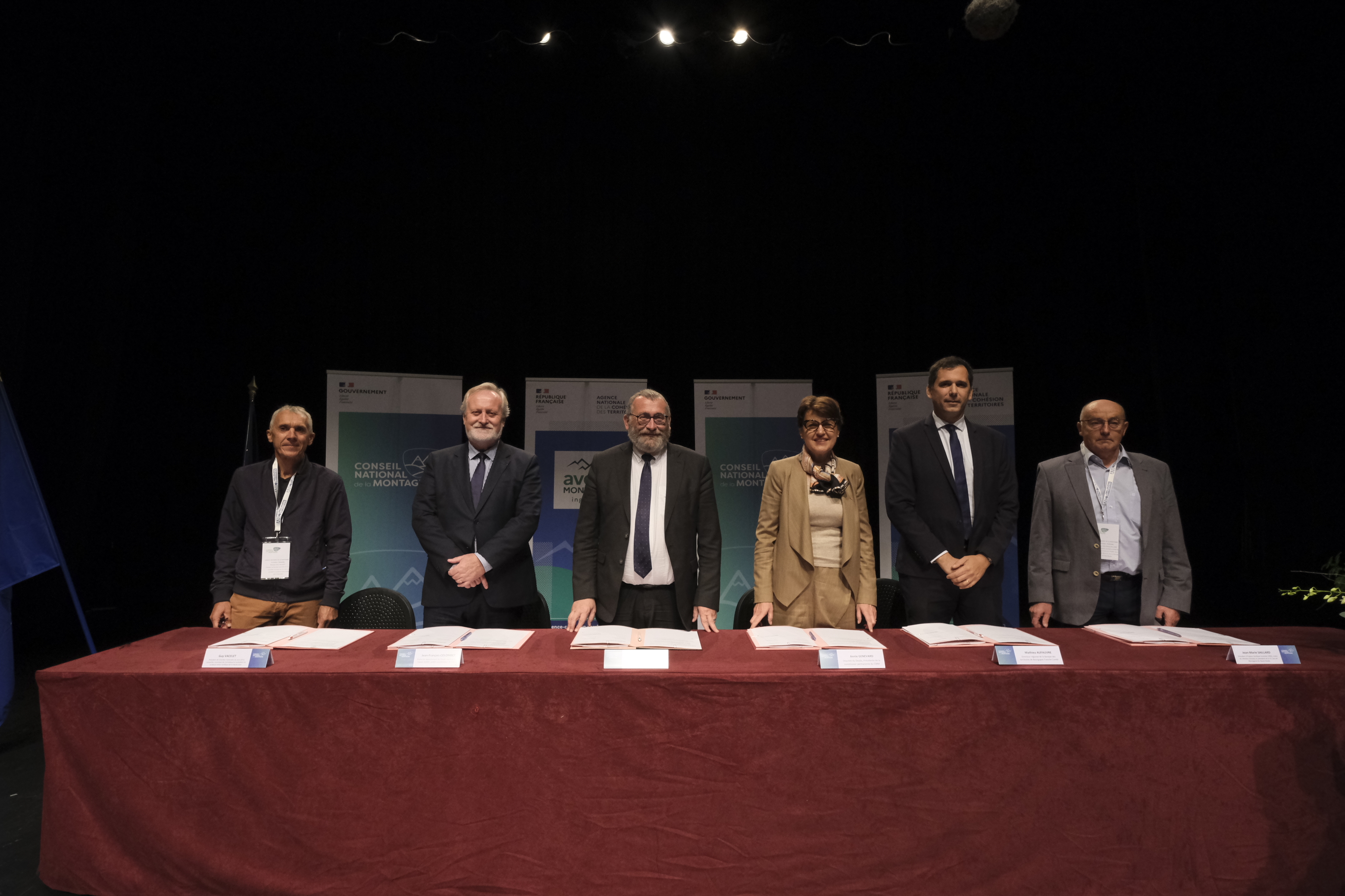 Des personnalit&eacute;s debout devant une table recouverte d'une nappe de velours rouge, avec le texte de la convention &agrave; signer devant eux