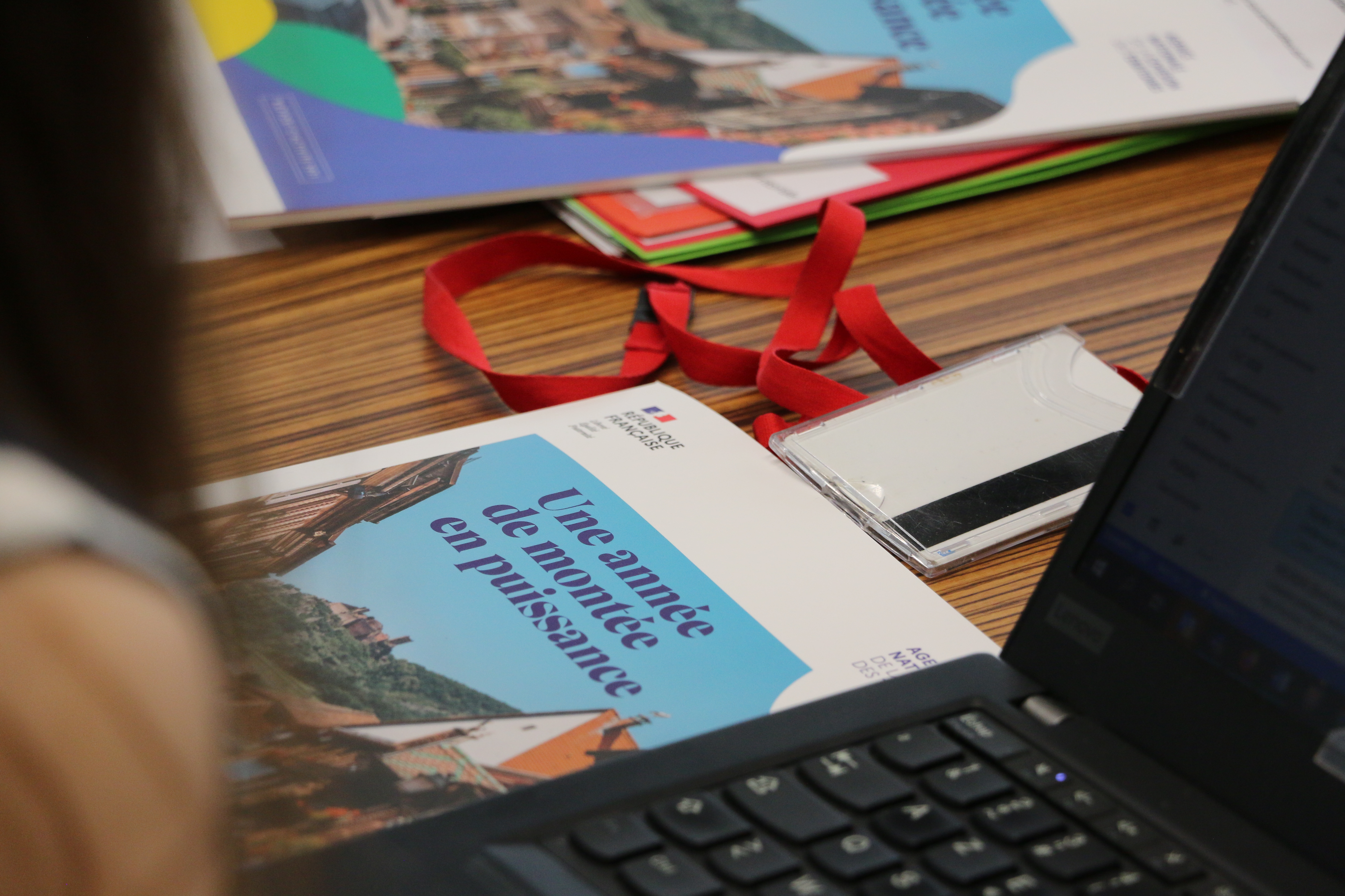 Gros plan sur la cuverture du rapport annuel pos&eacute; sur une table avec un ordinateur et une main au 1er plan.