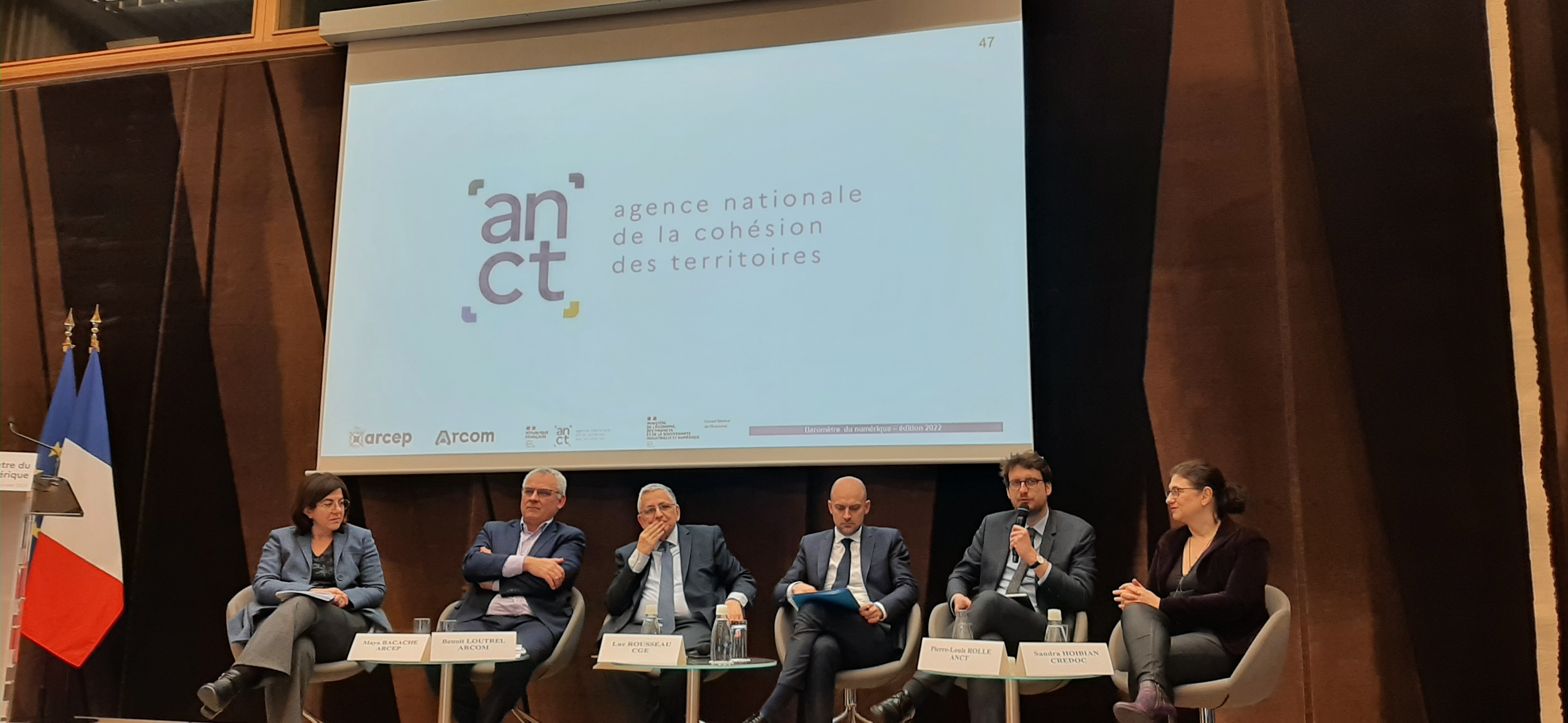 Conf&eacute;rence de presse, avec 2 femmes et 4 homes assis sur une sc&egrave;ne. Ils pr&eacute;sentent les r&eacute;sultats. Au-dessus d'eux, un grand &eacute;cran et, derri&egrave;re eux, un rideau rouge.