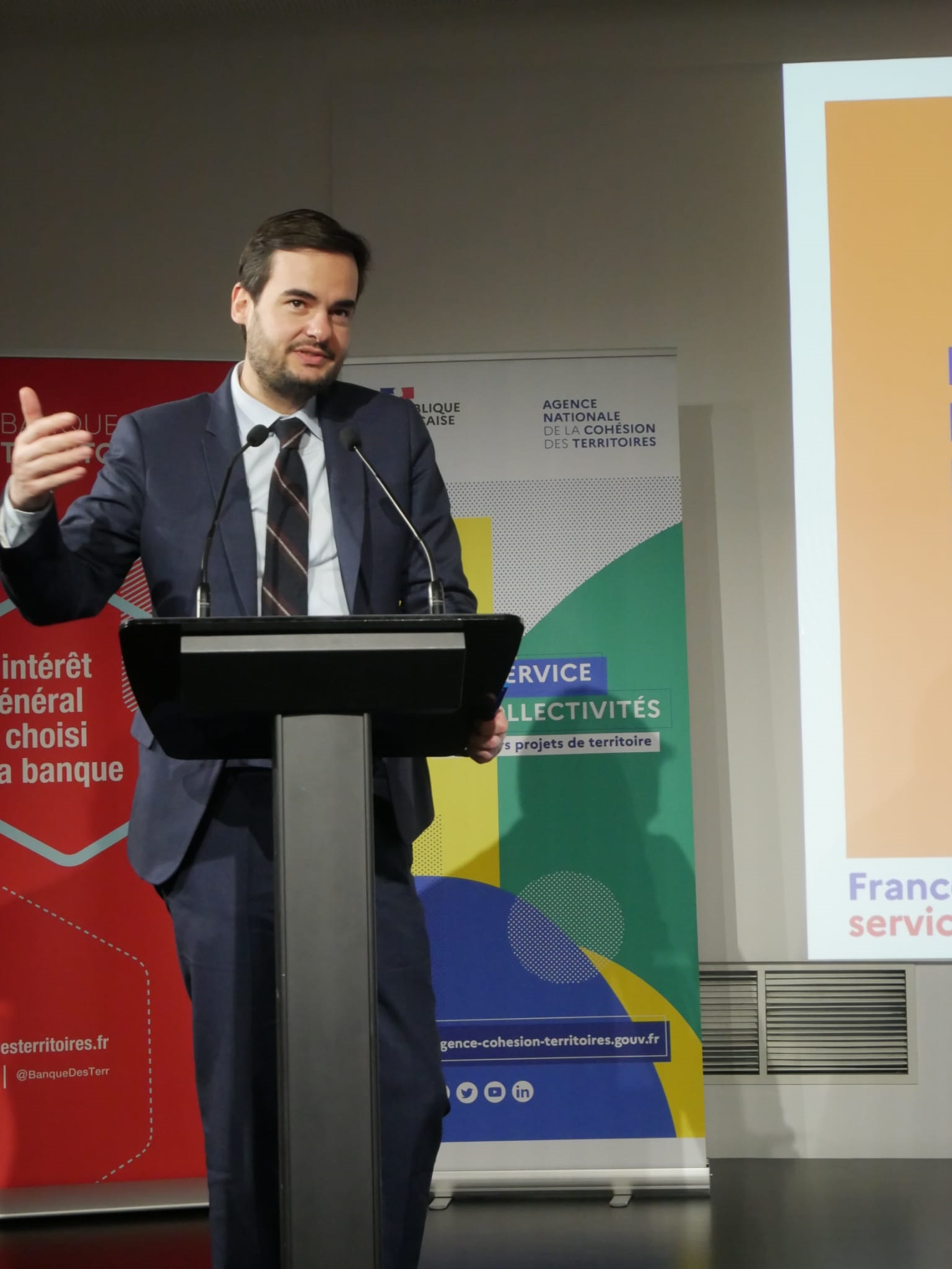 Intervenant debout sur une estrade, avec un pupitre et micro devant lui.