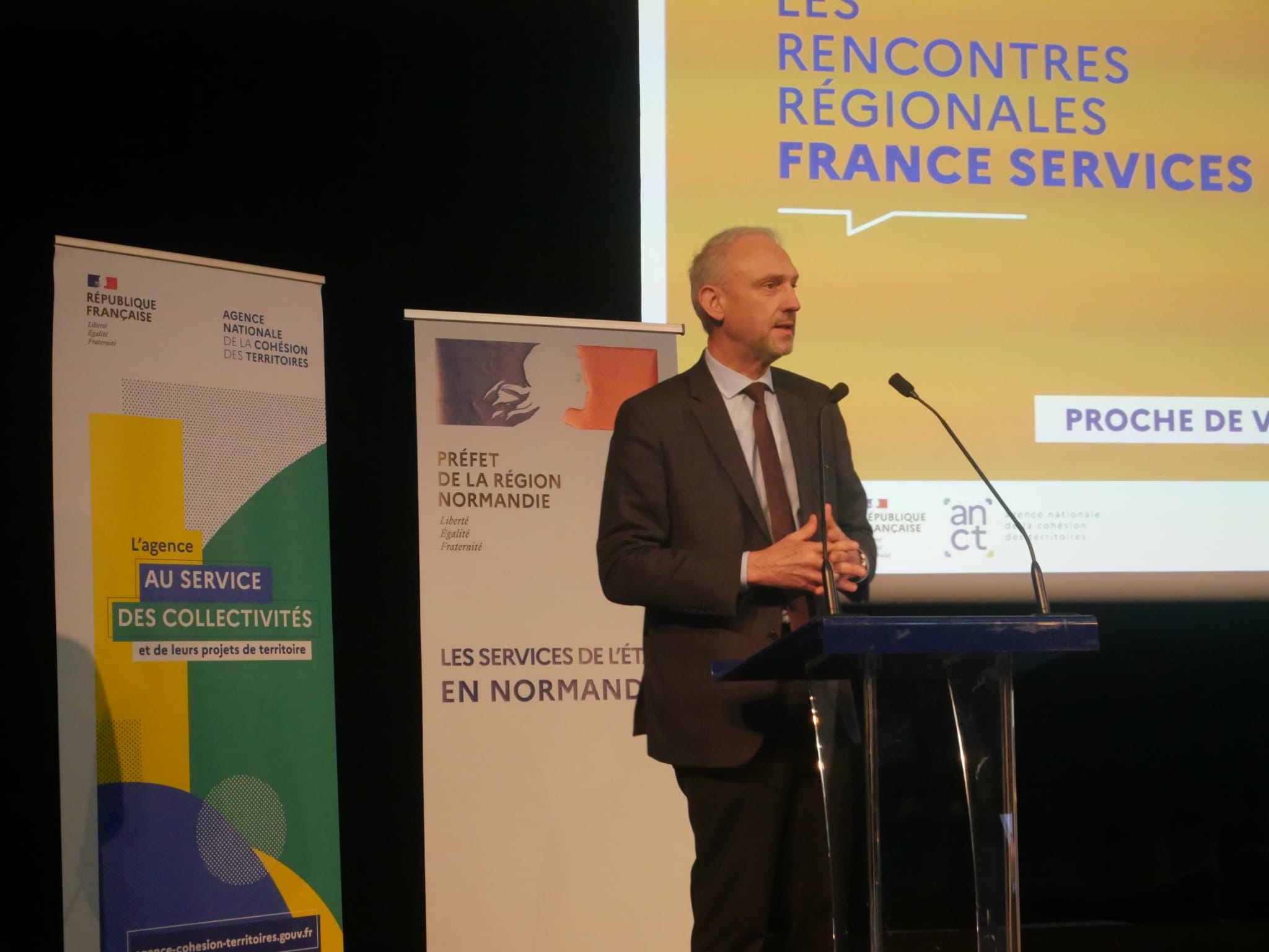 Un homme à la tribune, parle devant un micro.