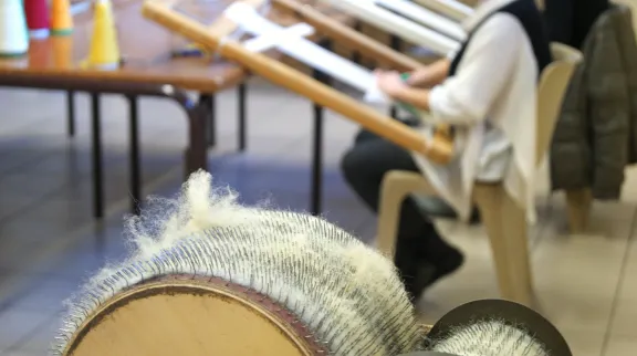 Vue sur des bobines de laine &agrave; filer, au 1er plan, et une artisan avec un m&eacute;tier &agrave; tisser traditionnel en bois, en arri&egrave;re plan.