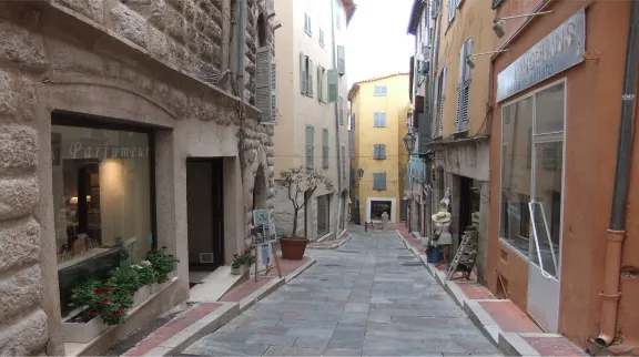 Vue d'une ruelle &eacute;troite, tr&egrave;s en pente, avec des boutiques et immeubles roses sur les c&ocirc;t&eacute;s. 